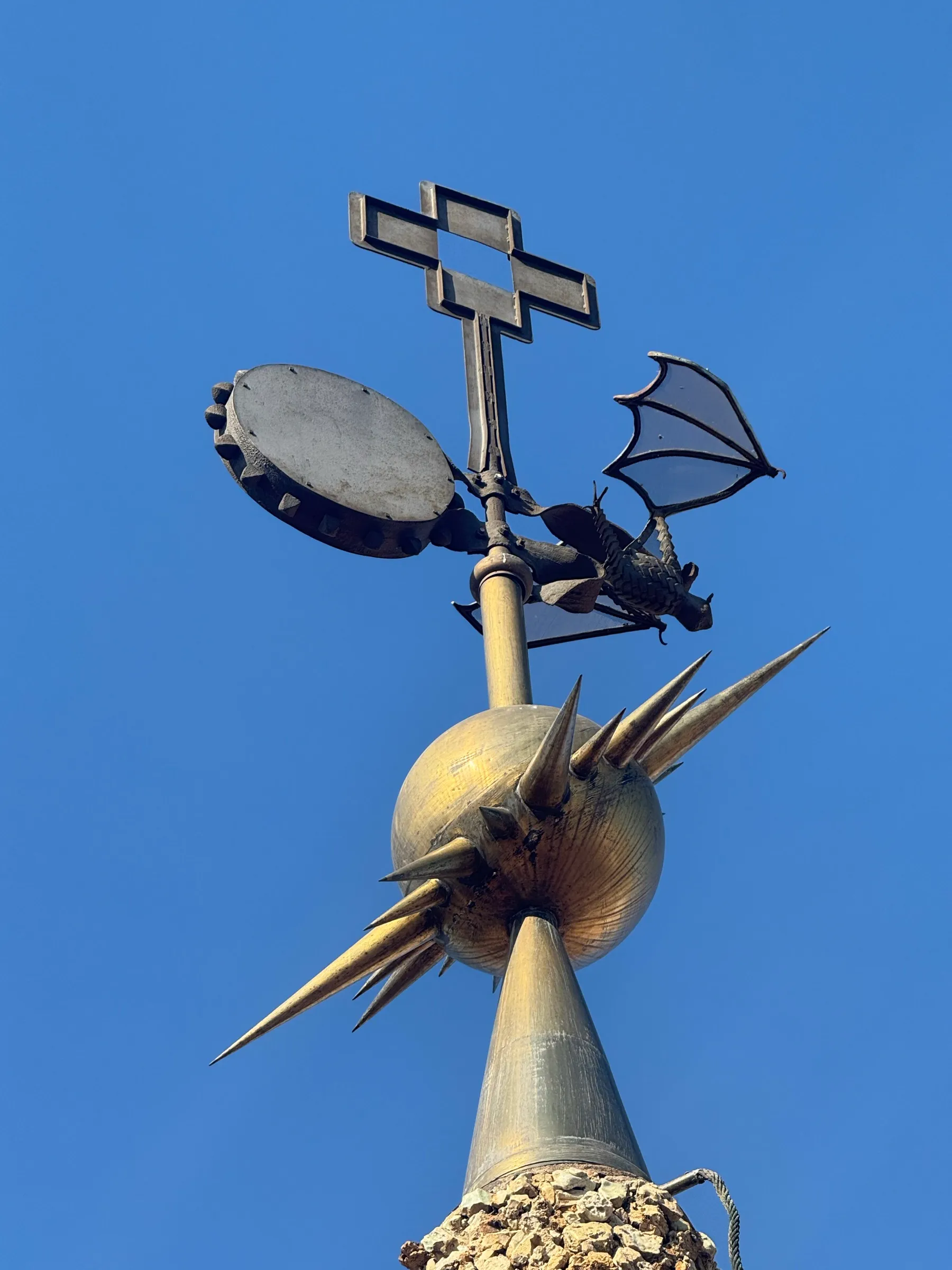 A wrought-iron winged dragon weathervane with a spiked golden finial against deep blue sky.