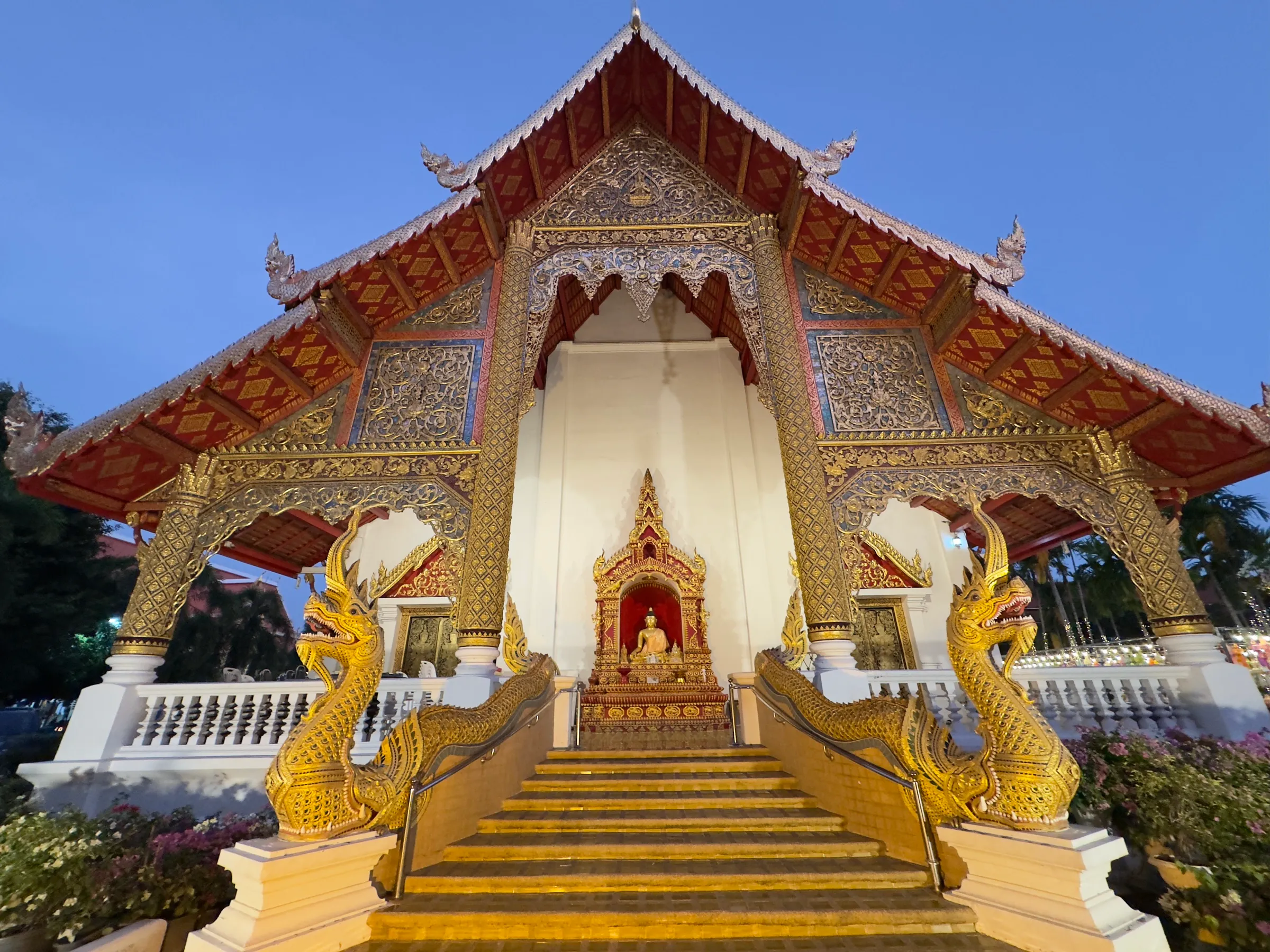 A golden Lanna temple at dusk, flanked by naga serpent balustrades.
