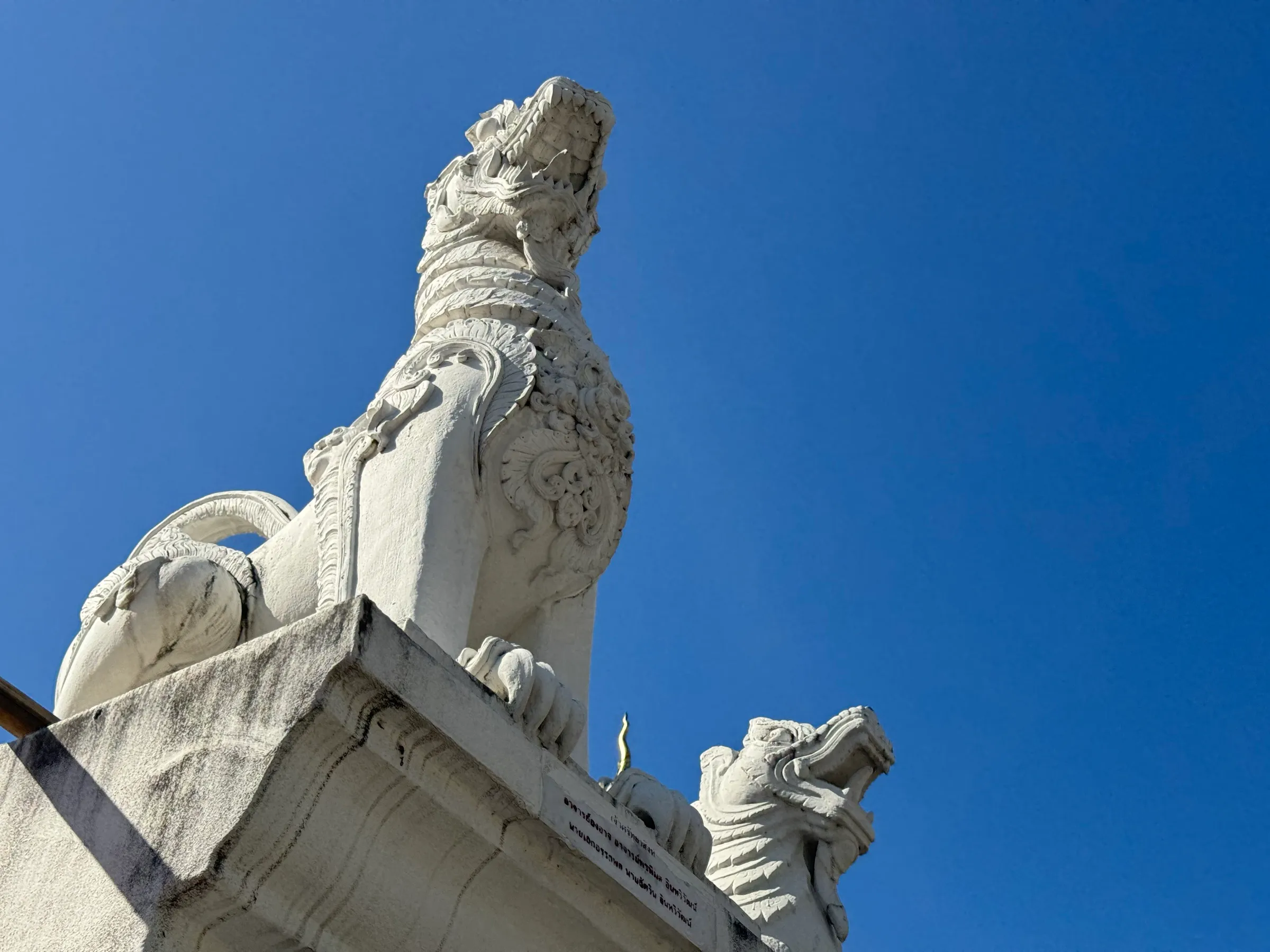 A white stone guardian singha statue at a temple against a clear blue sky.