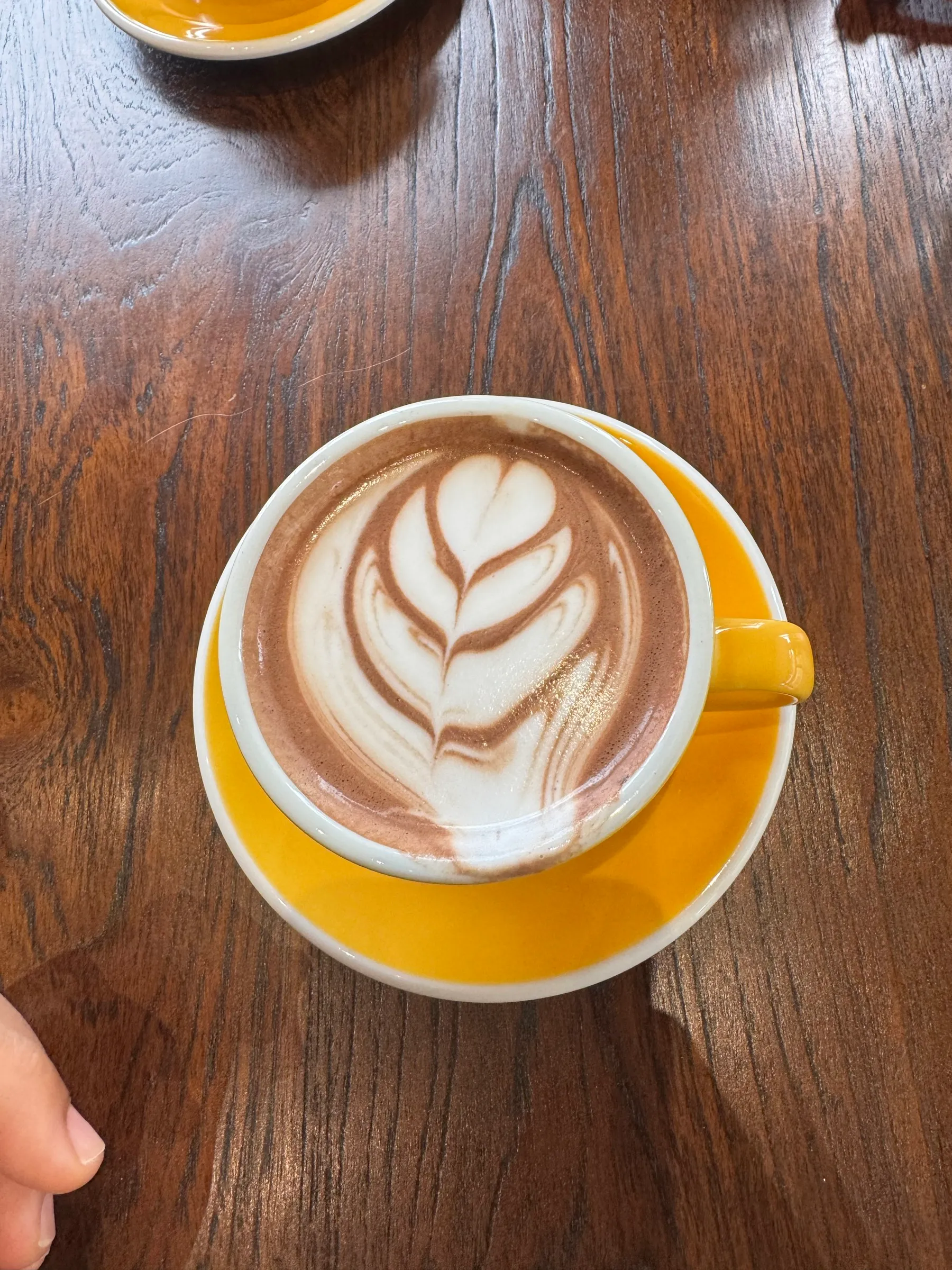 Leaf-shaped latte art in a yellow cup on a dark wood table.